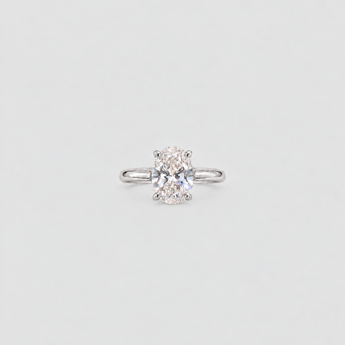 A single solitaire engagement ring featuring a round brilliant-cut diamond set in a polished silver-colored band, centered on a light gray background.