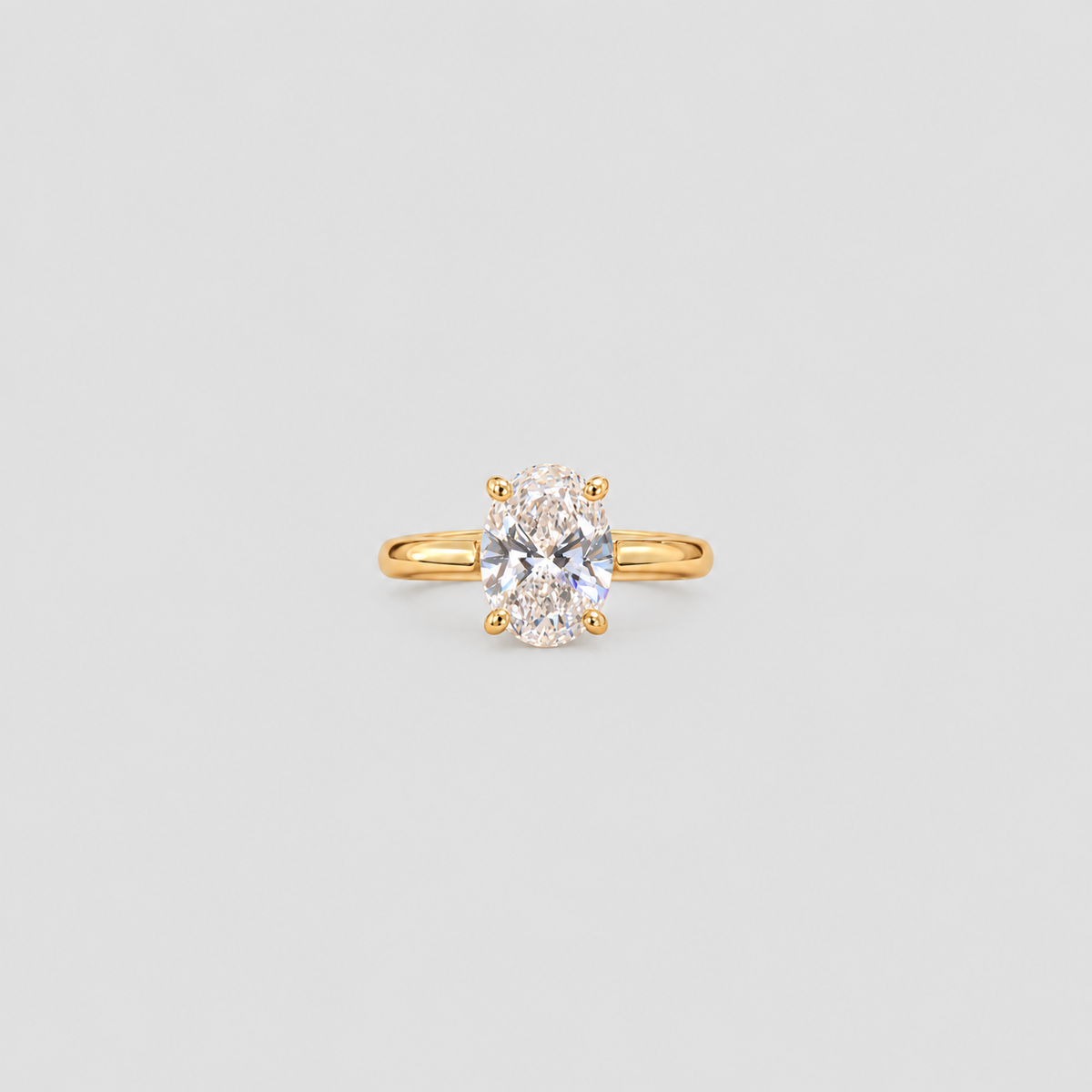 A yellow gold solitaire ring featuring an oval-cut clear gemstone in a four-prong setting, centered on a light gray background.