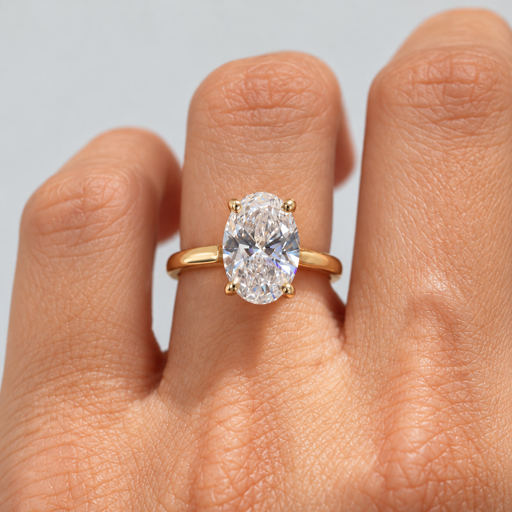 A close-up of a hand wearing a yellow gold ring with an oval-cut clear gemstone in a four-prong setting, set against a light gray background.