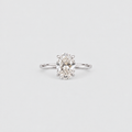 A classic solitaire engagement ring featuring an oval-cut diamond set in a polished silver-colored metal band, centered on a light gray background.