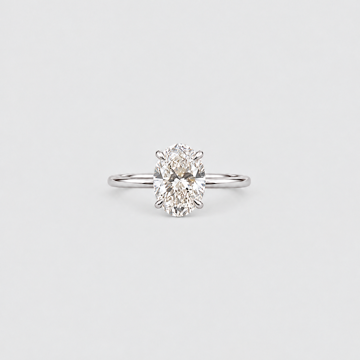 A classic solitaire engagement ring featuring an oval-cut diamond set in a polished silver-colored metal band, centered on a light gray background.