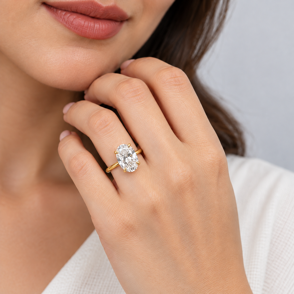 A close-up lifestyle shot of a woman wearing a yellow gold ring with an oval-cut clear gemstone on her finger.