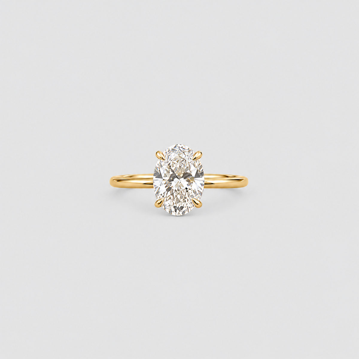 A yellow gold solitaire ring featuring an oval-cut diamond in a four-prong setting, centered on a light gray background.