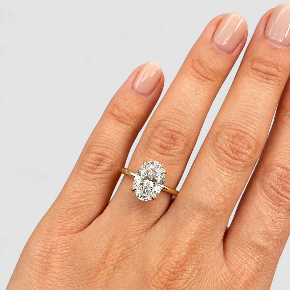 A close-up of a hand wearing a yellow gold ring with a large oval-cut diamond. The diamond is set in a prong setting on a slim gold band.