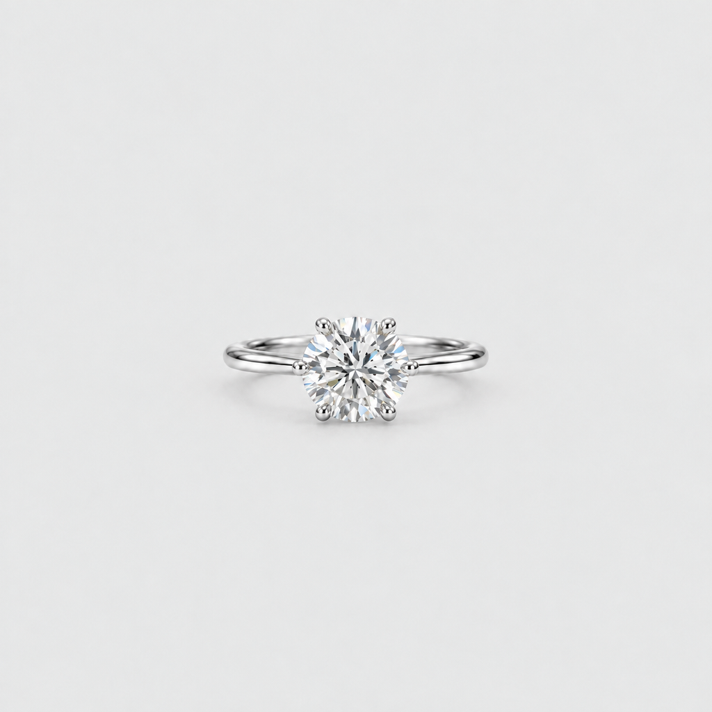 A classic solitaire engagement ring featuring a round brilliant-cut diamond set in a polished silver-colored metal band, centered on a light gray background.