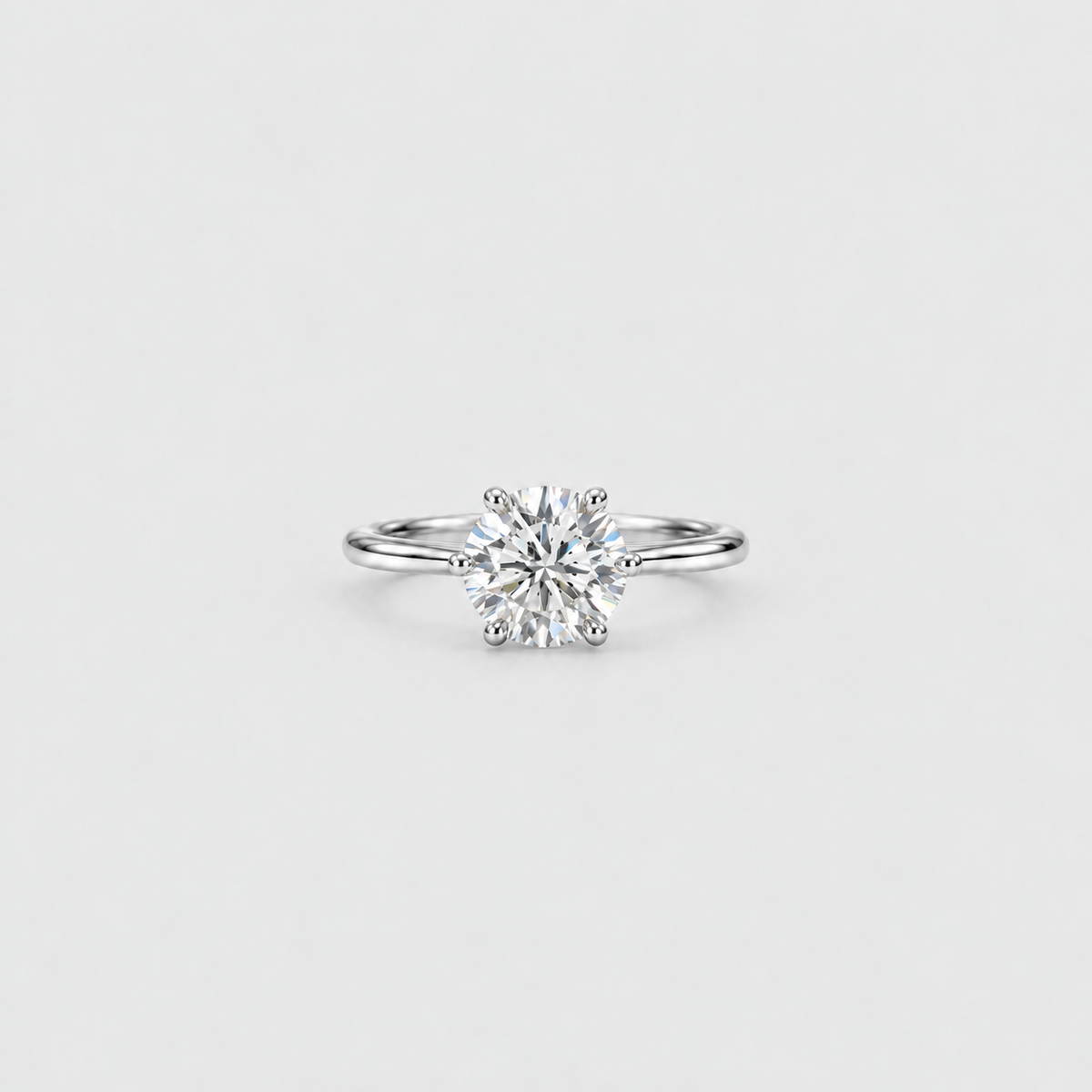 A classic solitaire engagement ring featuring a round brilliant-cut diamond set in a polished silver-colored metal band, centered on a light gray background.