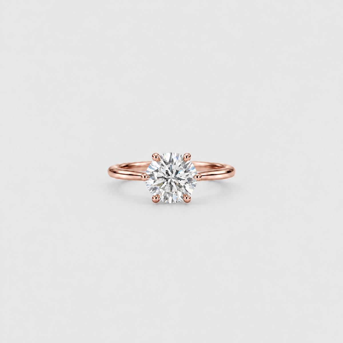 A classic solitaire engagement ring featuring a round brilliant-cut diamond set in a rose gold four-prong band, centered on a light gray background.