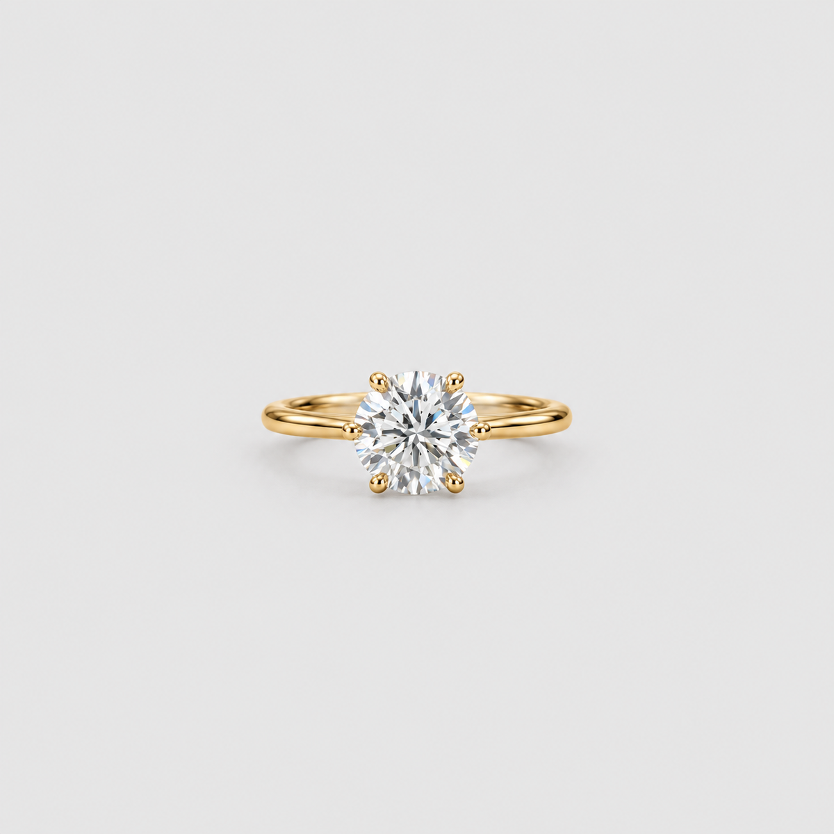 A classic solitaire engagement ring featuring a round brilliant-cut diamond set in a yellow gold band with a four-prong setting, centered on a light gray background.