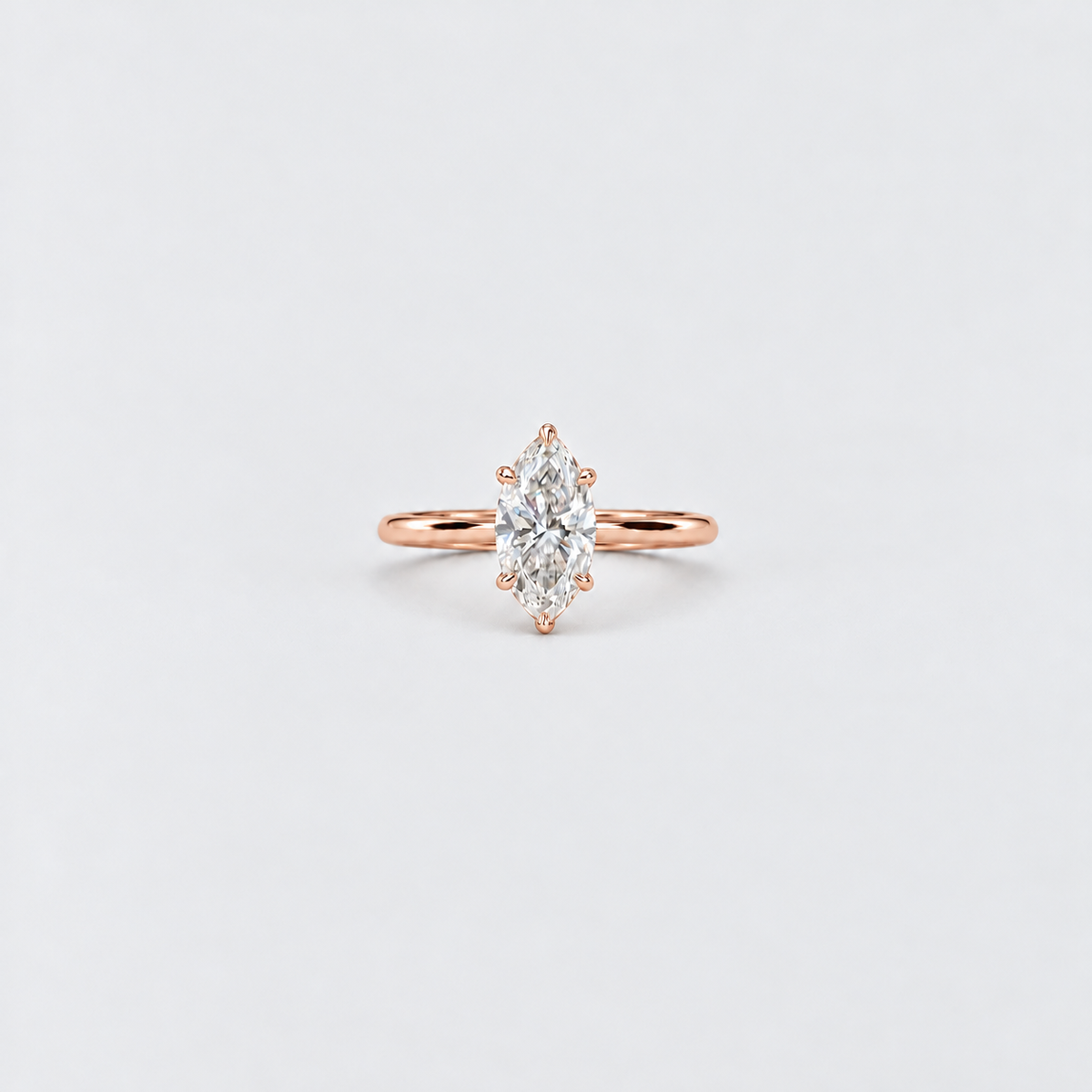 A rose gold ring featuring a marquise-cut diamond center stone in a prong setting, shown on a clean, light gray background.