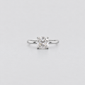 A classic solitaire engagement ring featuring a brilliant round-cut diamond set in a polished silver-colored band, centered against a light gray background.
