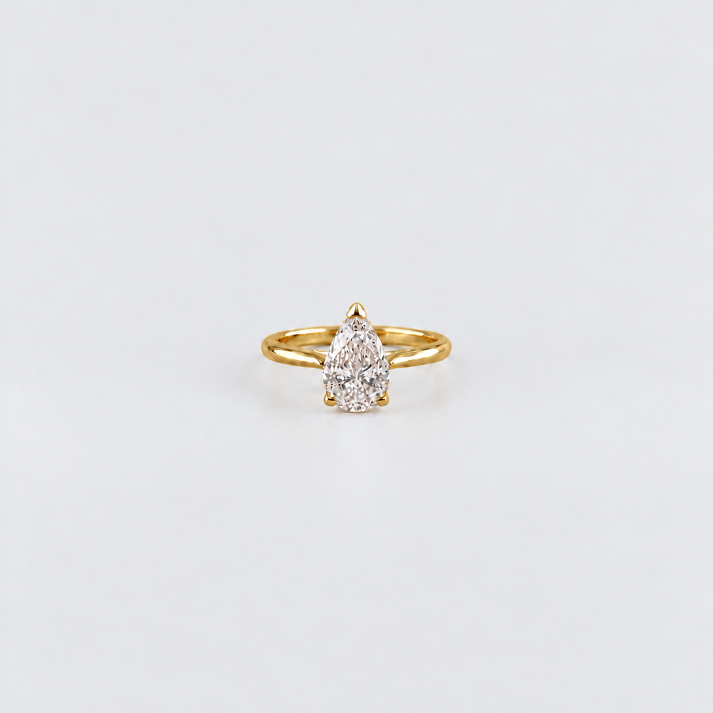 A yellow gold ring featuring a pear-cut clear gemstone in a four-prong setting, centered on a clean white background.
