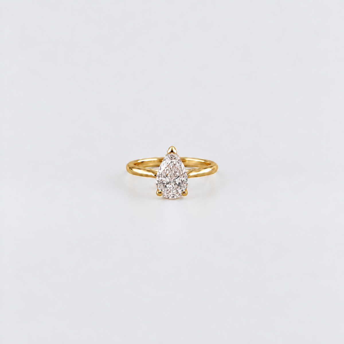 A yellow gold ring featuring a pear-cut clear gemstone in a four-prong setting, centered on a clean white background.