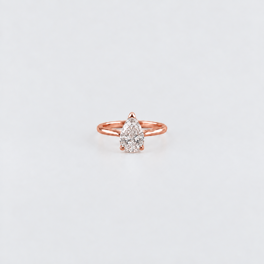 A pear-cut diamond ring in a rose gold setting, centered on a clean, light gray background.