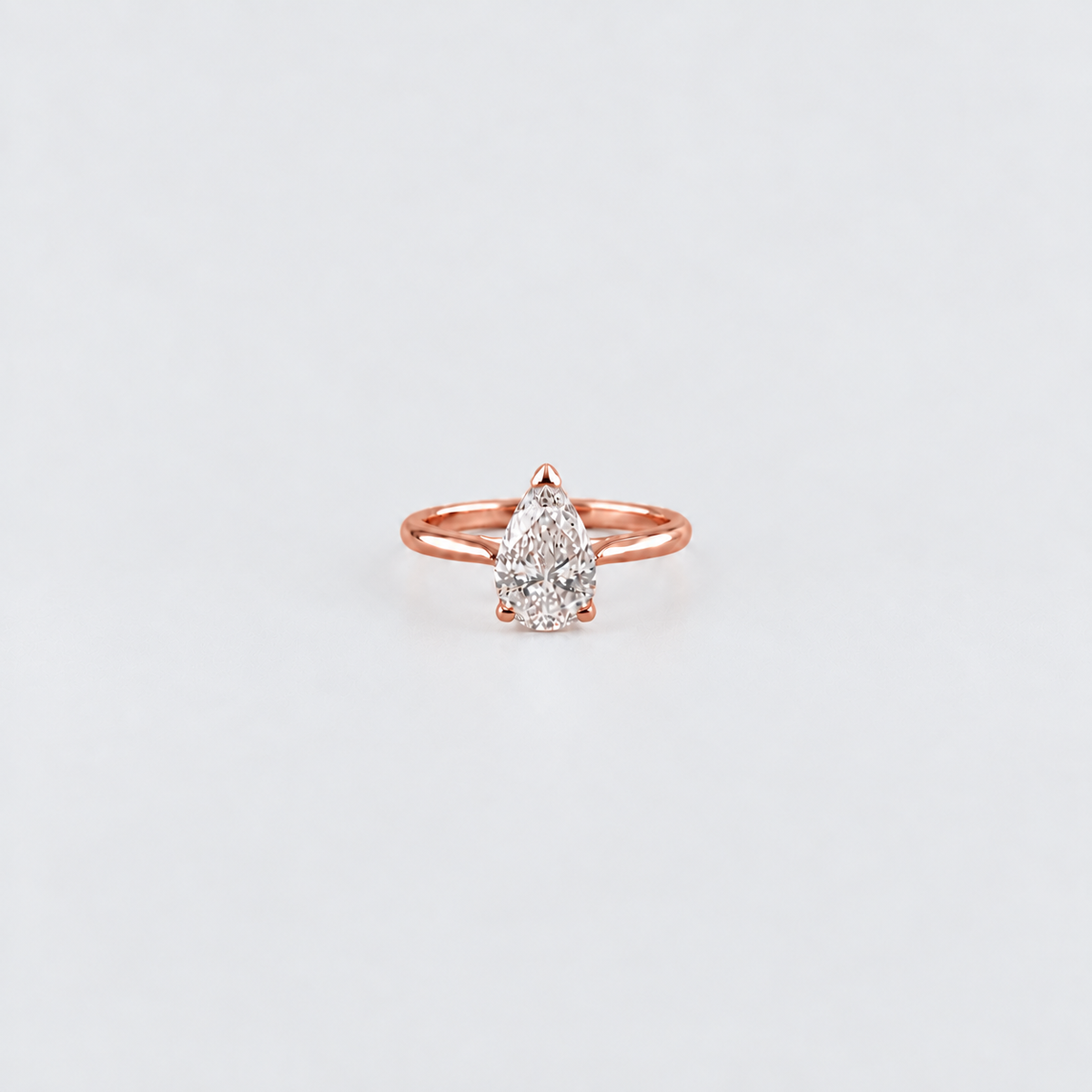 A pear-cut diamond ring in a rose gold setting, centered on a clean, light gray background.