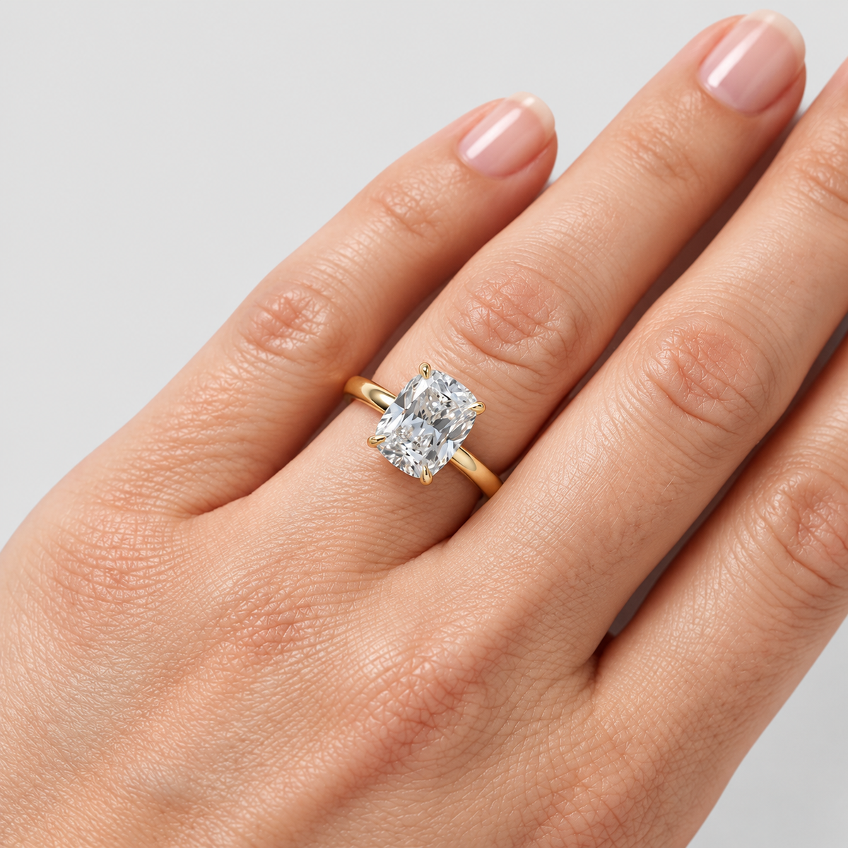 A close-up of a hand wearing a yellow gold ring with a large rectangular clear gemstone, set against a plain light gray background.