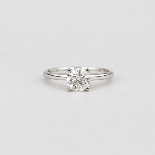 A classic solitaire engagement ring featuring a round brilliant-cut diamond set in a four-prong silver band, photographed on a clean, light gray background.