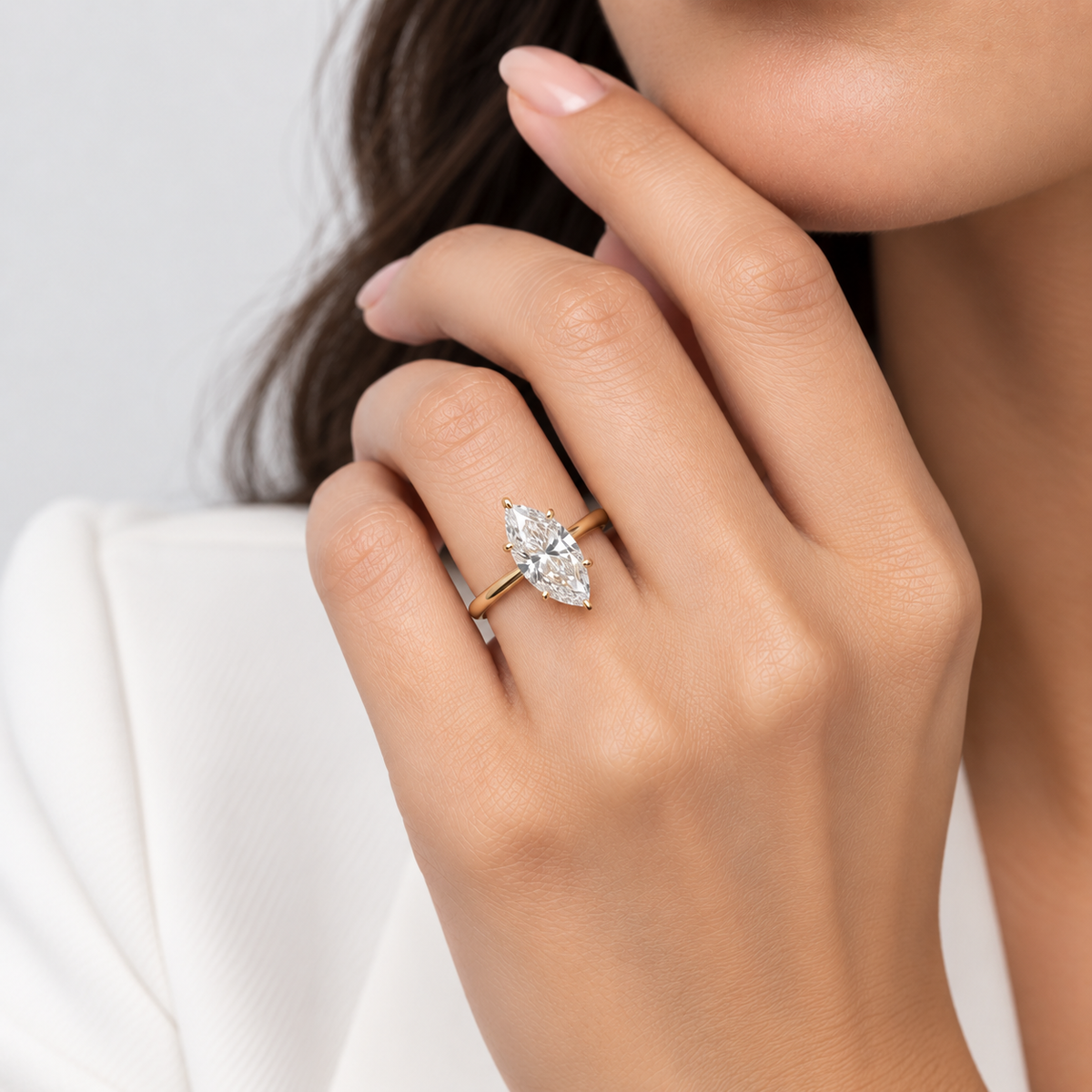 A close-up lifestyle shot of a woman wearing a yellow gold ring with a marquise-cut clear gemstone on her finger.