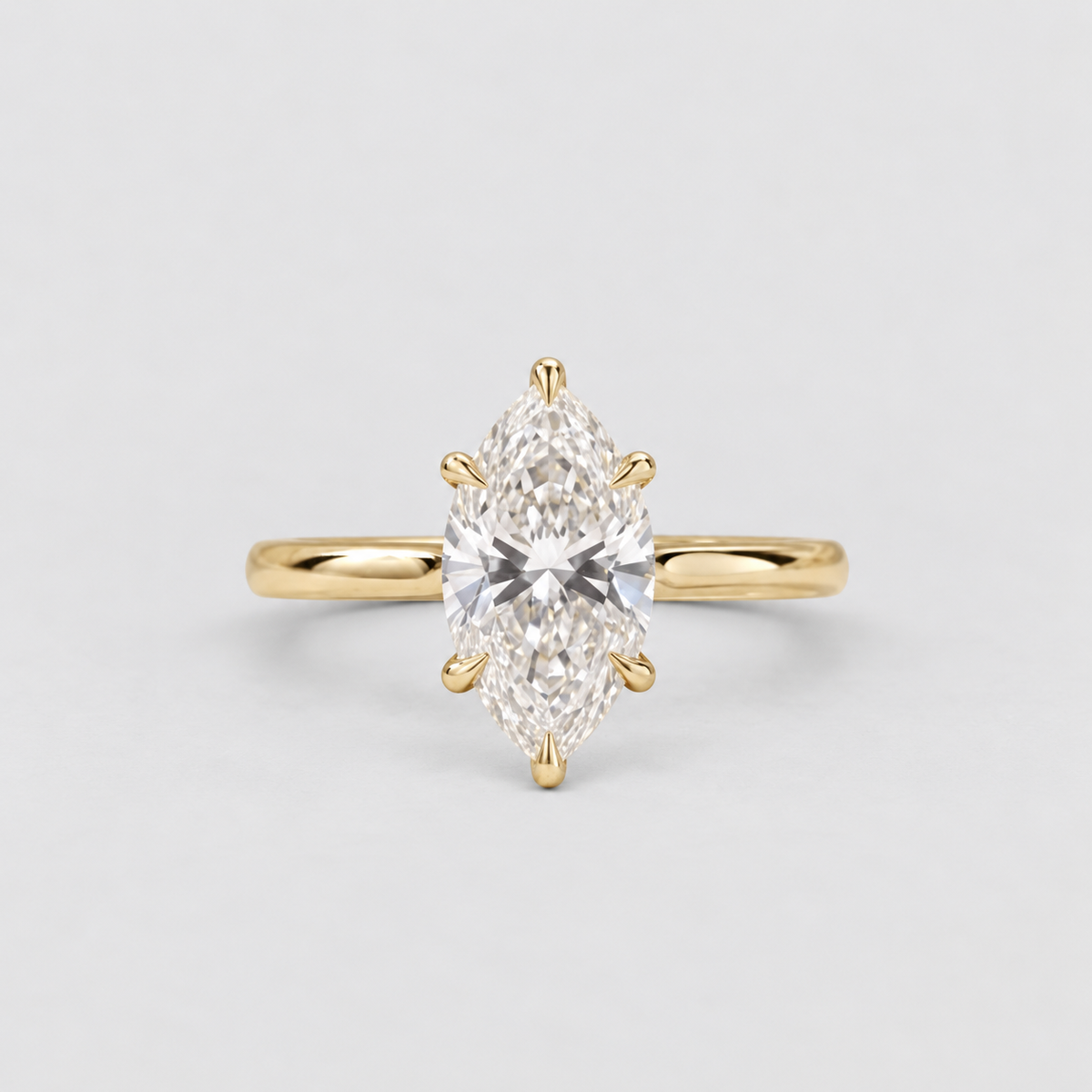 A yellow gold ring featuring a marquise-cut diamond center stone in a six-prong setting, shown against a clean, light gray background.