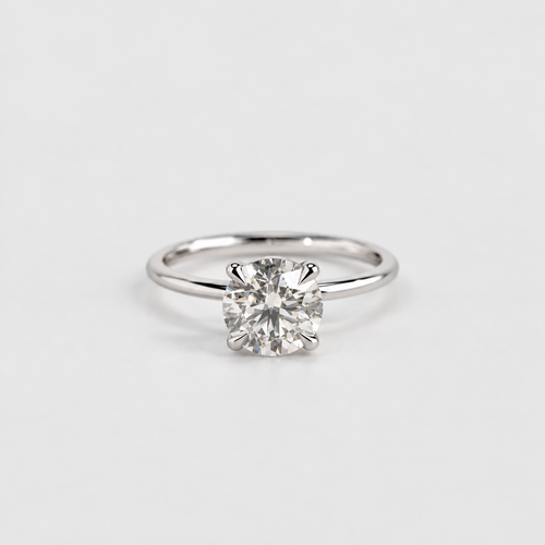 A classic solitaire engagement ring featuring a round brilliant-cut diamond set in a polished white gold or platinum band, photographed on a clean, light gray background.
