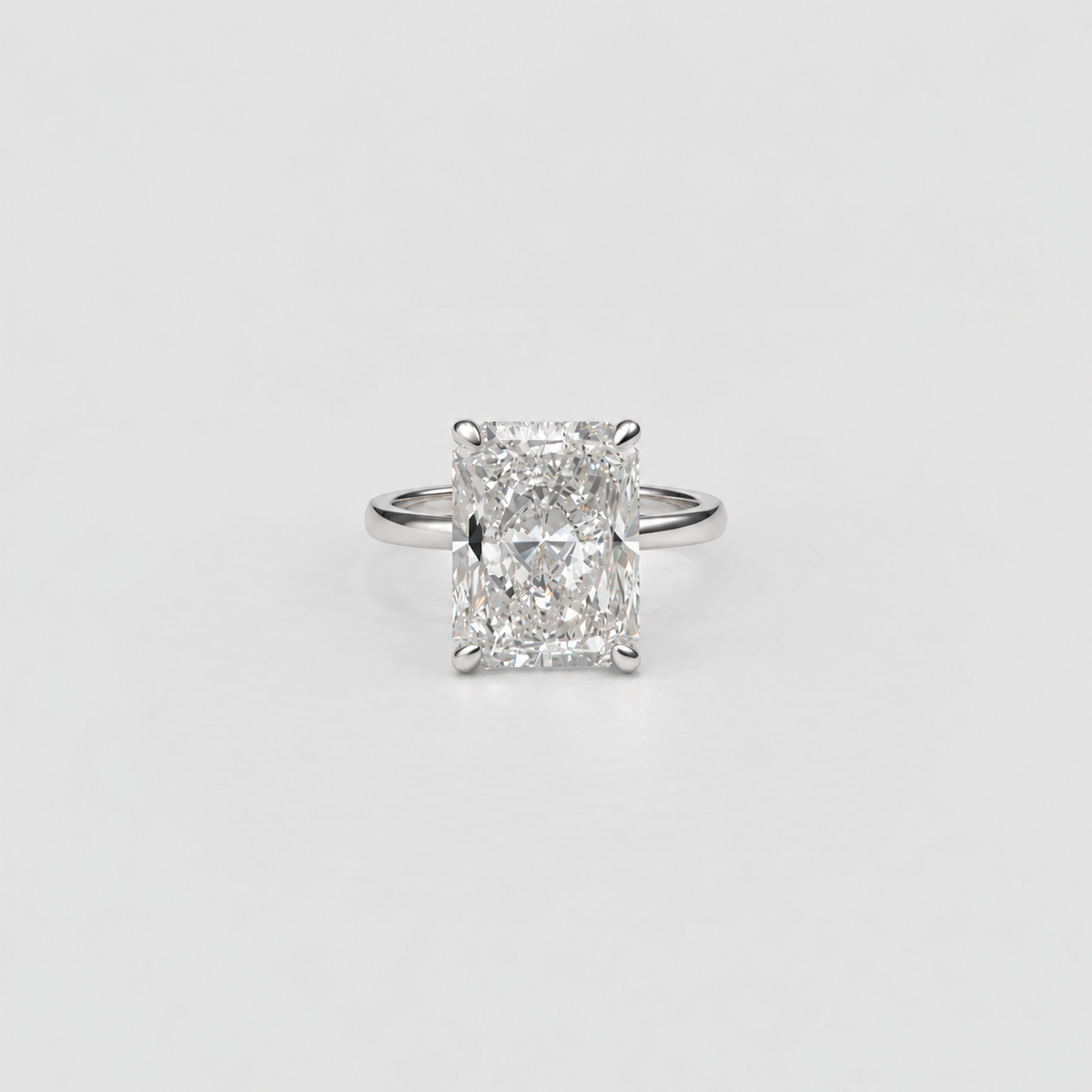 An emerald-cut diamond ring with a silver-toned band, centered on a clean, light gray background.