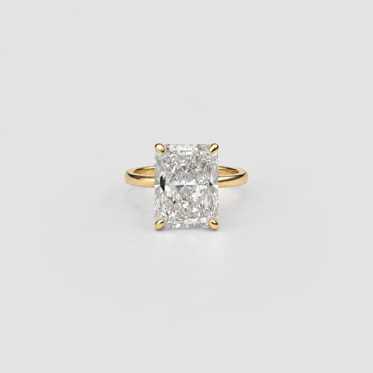 An emerald-cut diamond ring in a yellow gold four-prong setting, centered on a light gray background.