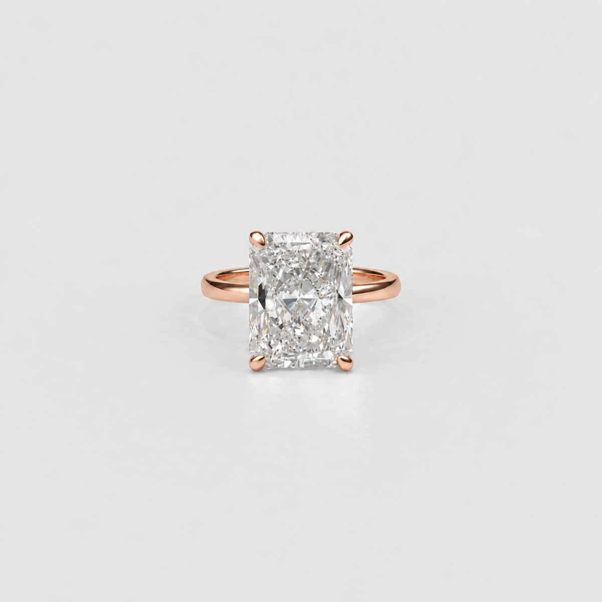 A radiant cut diamond ring set in a rose gold band, photographed against a clean, light gray background.