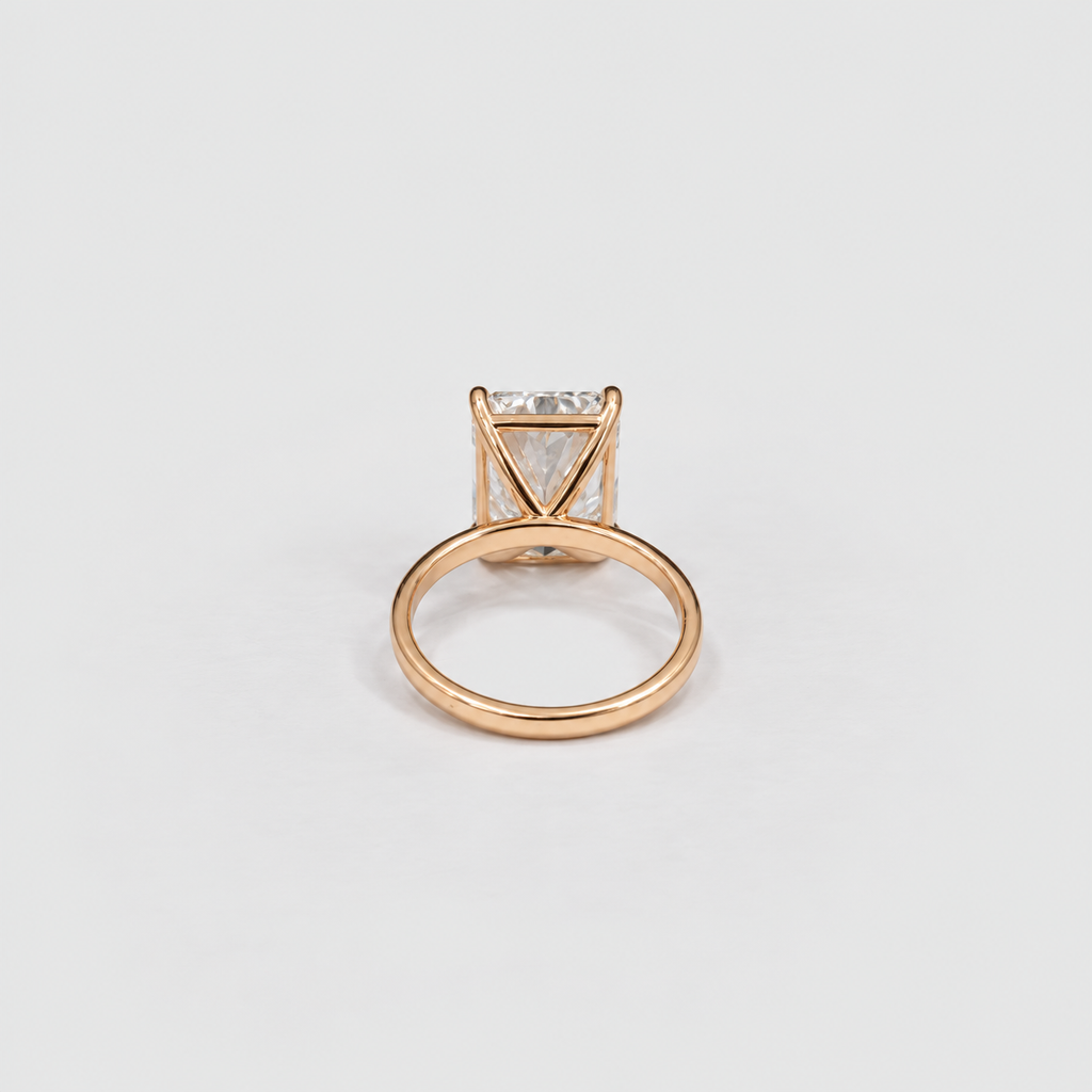 A rose gold ring with a triangular prong setting holding a clear rectangular gemstone, shown on a clean light gray background.