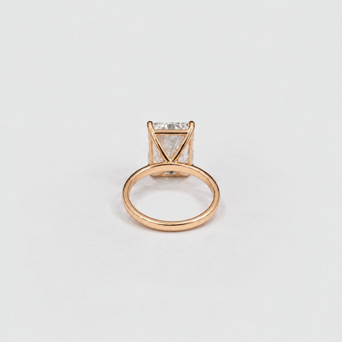 A rose gold ring with a triangular prong setting holding a clear rectangular gemstone, shown on a clean light gray background.