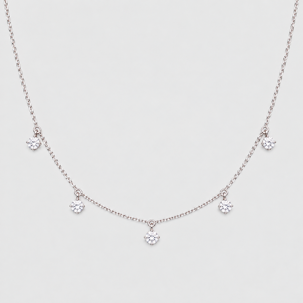 A delicate silver-tone necklace featuring a fine chain with five small, clear crystal flower-like charms spaced along the front, displayed against a light gray background.