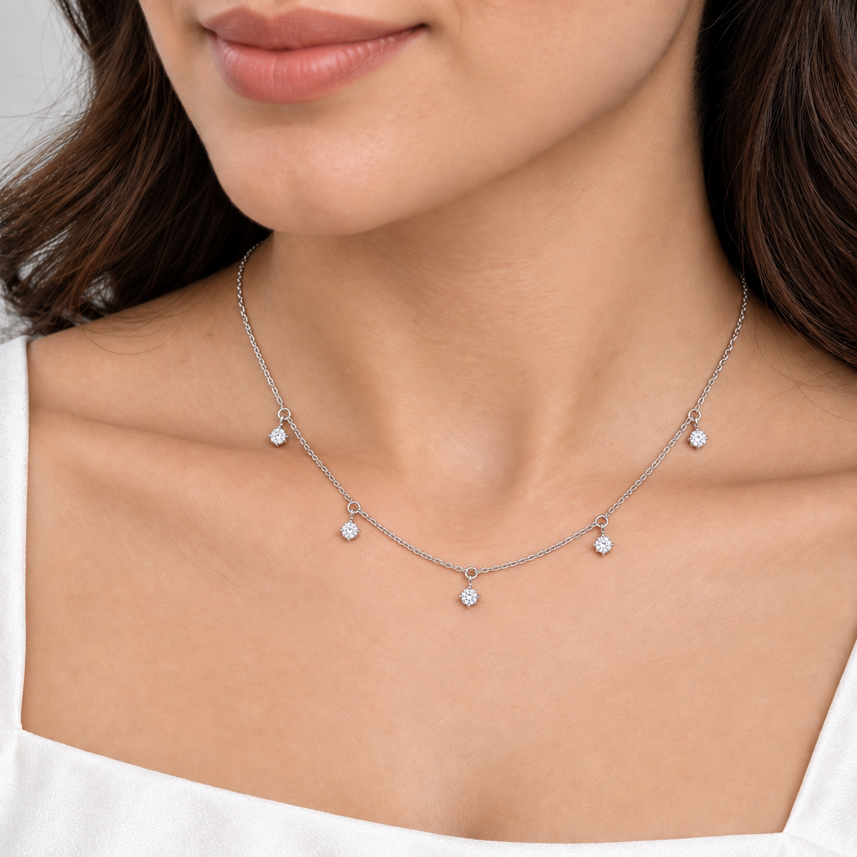 A close-up of a model wearing a delicate silver chain necklace with five small, clear round-cut gemstone pendants.