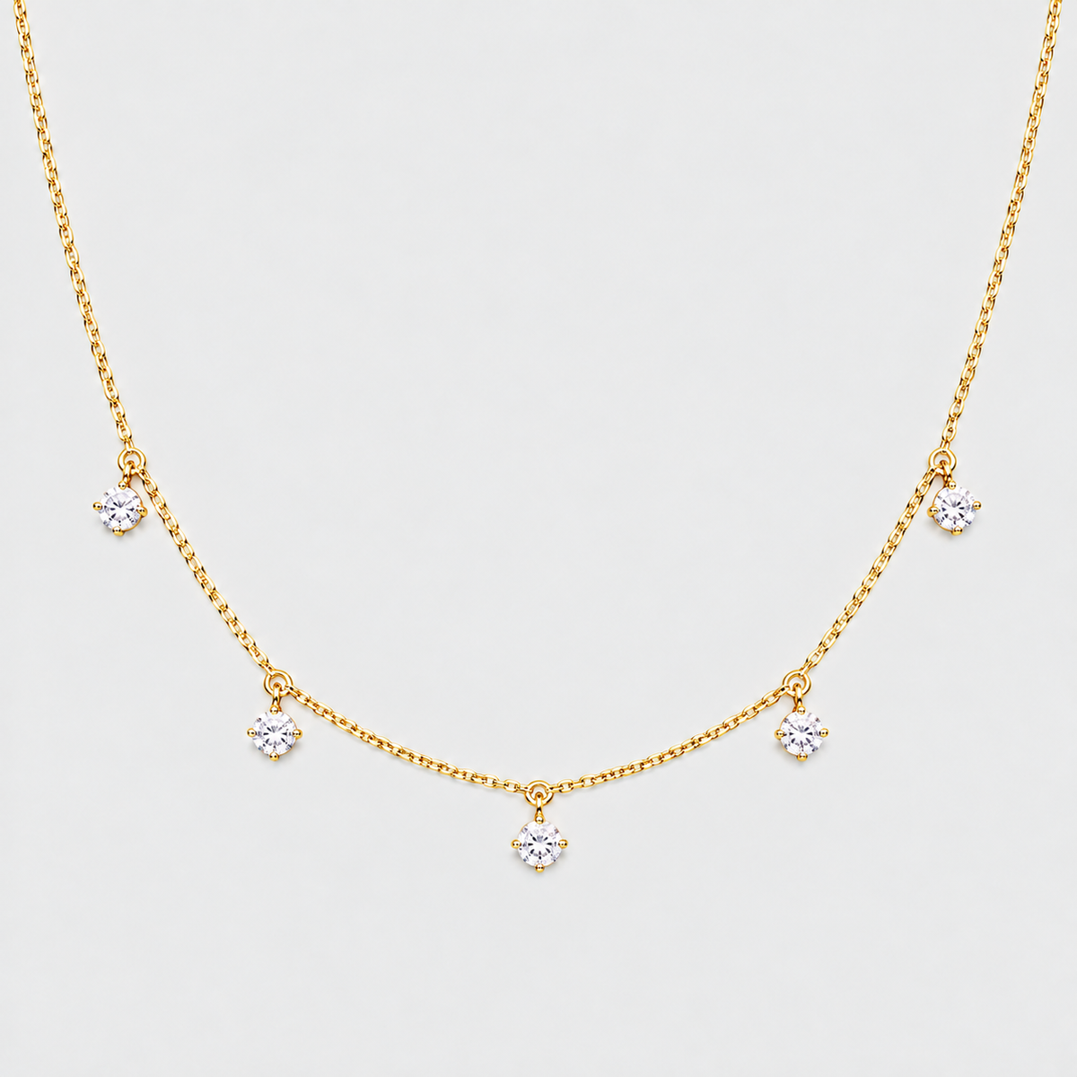 A delicate gold chain necklace featuring five small, clear flower-shaped crystal charms spaced along the chain, displayed against a light gray background.