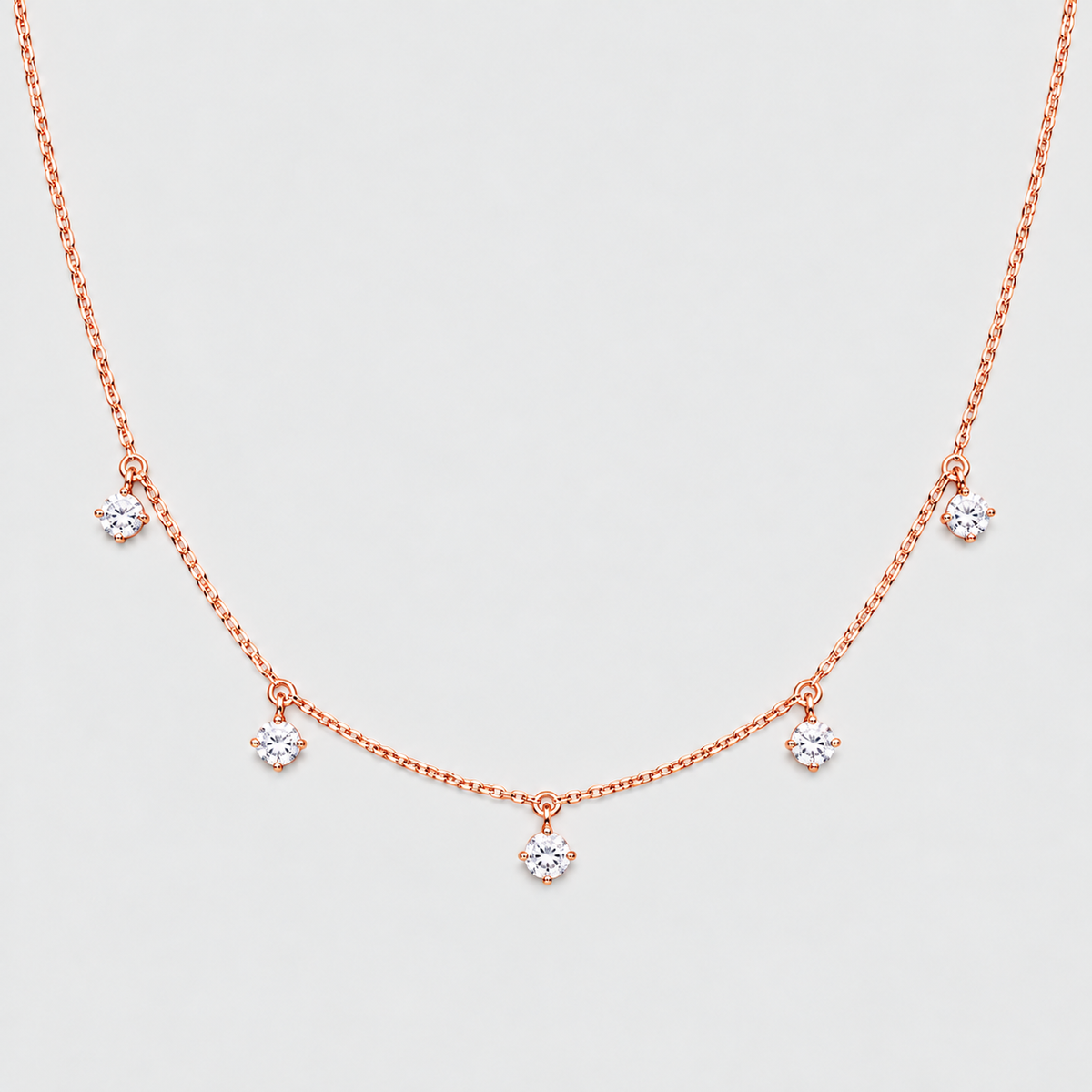 A delicate rose gold necklace with five small flower-shaped crystal charms spaced along a fine chain, displayed against a light gray background.