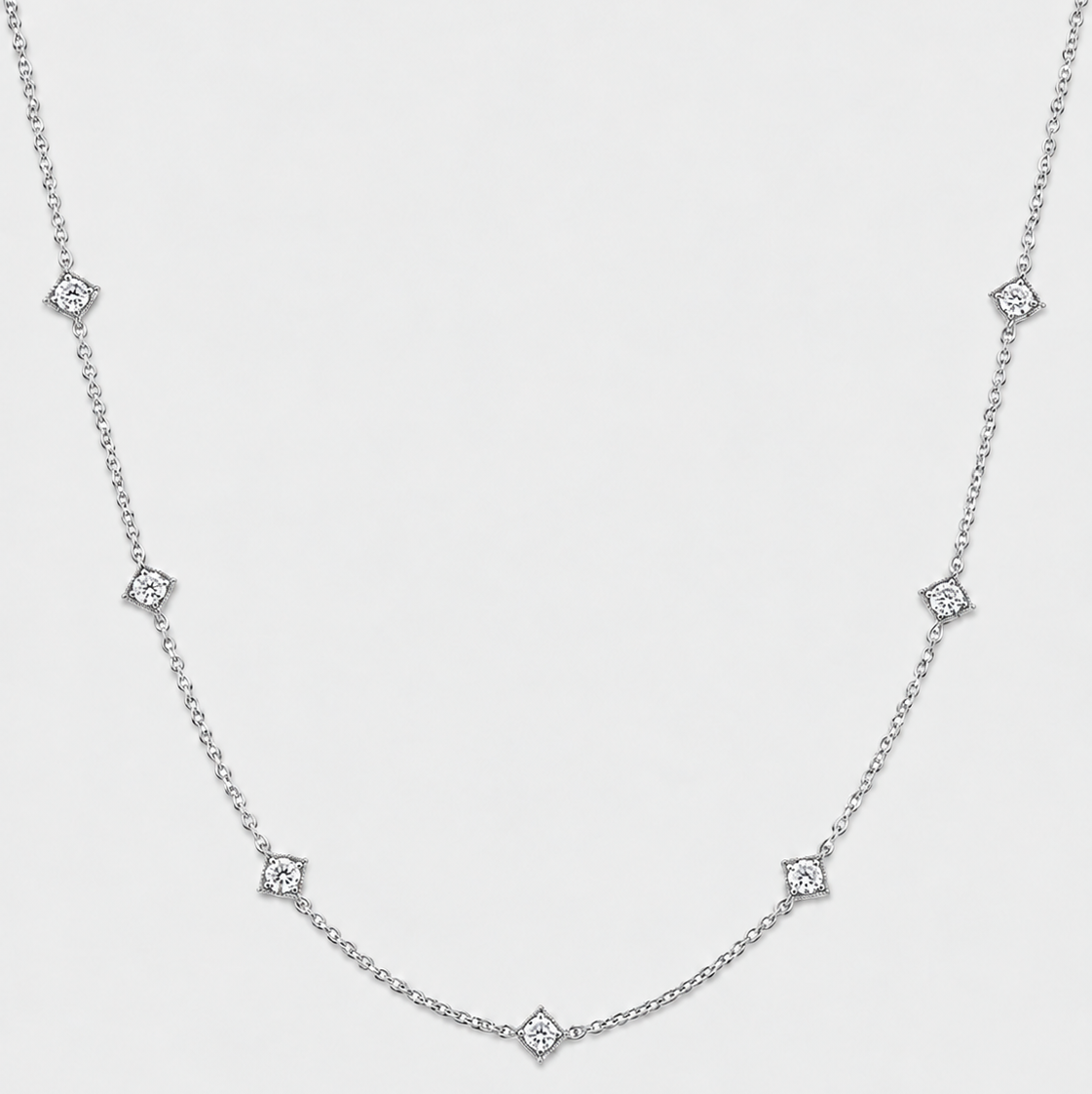 A delicate silver chain necklace featuring small diamond-shaped diamond accents spaced along the chain, photographed against a light gray background.
