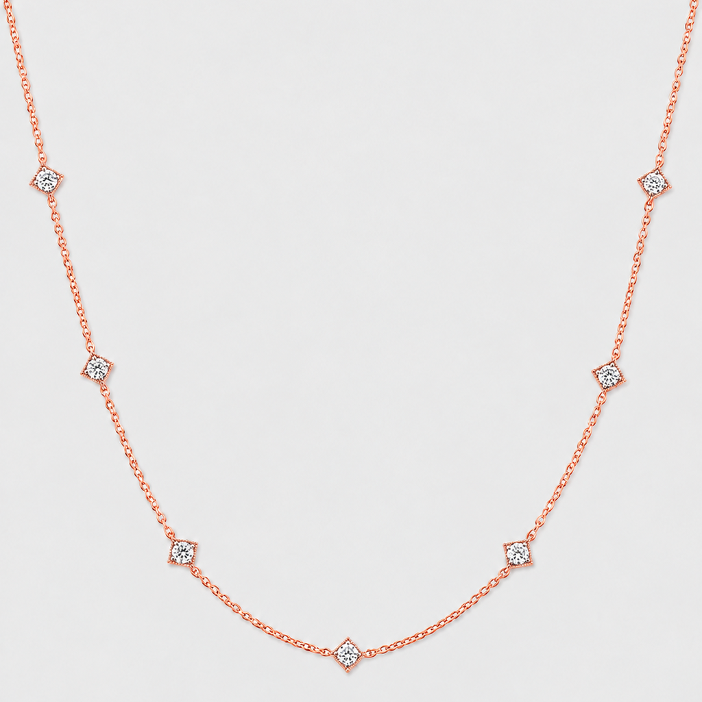 A delicate rose gold chain necklace featuring small diamond-shaped settings with clear round-cut stones, arranged in a gentle U-shape against a light gray background.