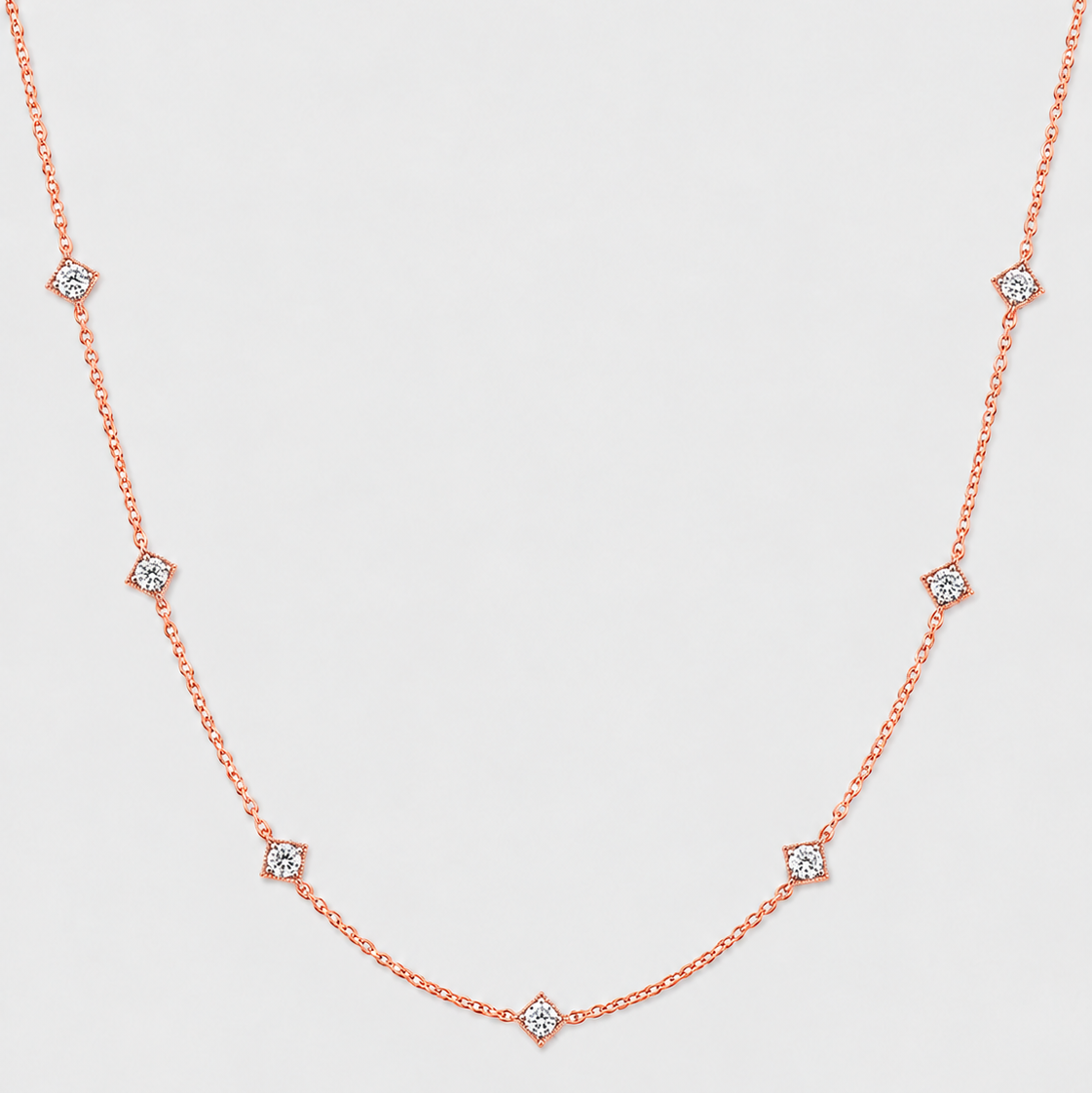 A delicate rose gold chain necklace featuring small diamond-shaped settings with clear round-cut stones, arranged in a gentle U-shape against a light gray background.