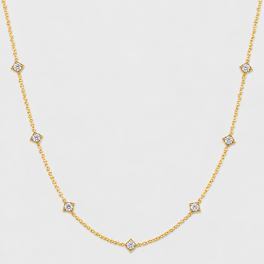 A delicate gold chain necklace featuring seven small diamond-shaped settings with clear stones, arranged in a gentle curve on a light gray background.