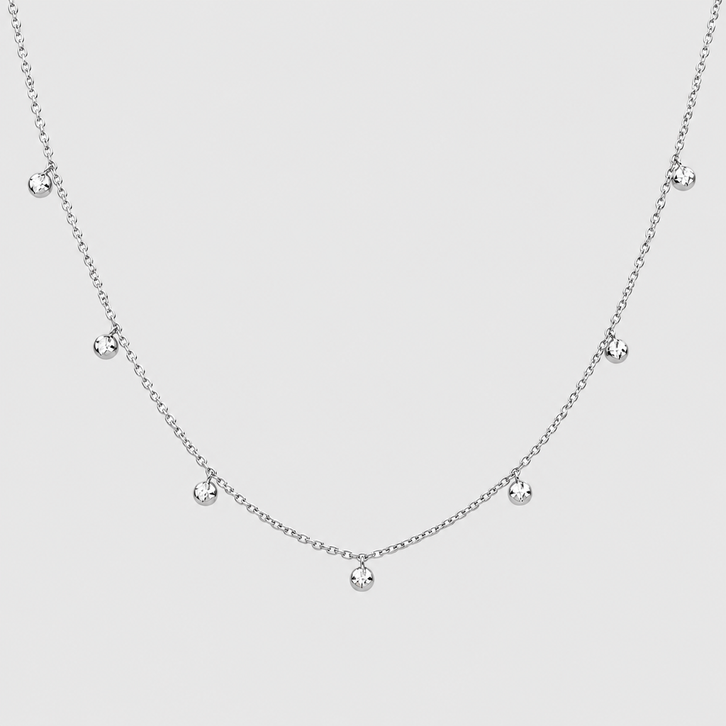 A delicate silver chain necklace featuring seven small, clear round gemstones spaced along the chain, displayed against a solid light gray background.
