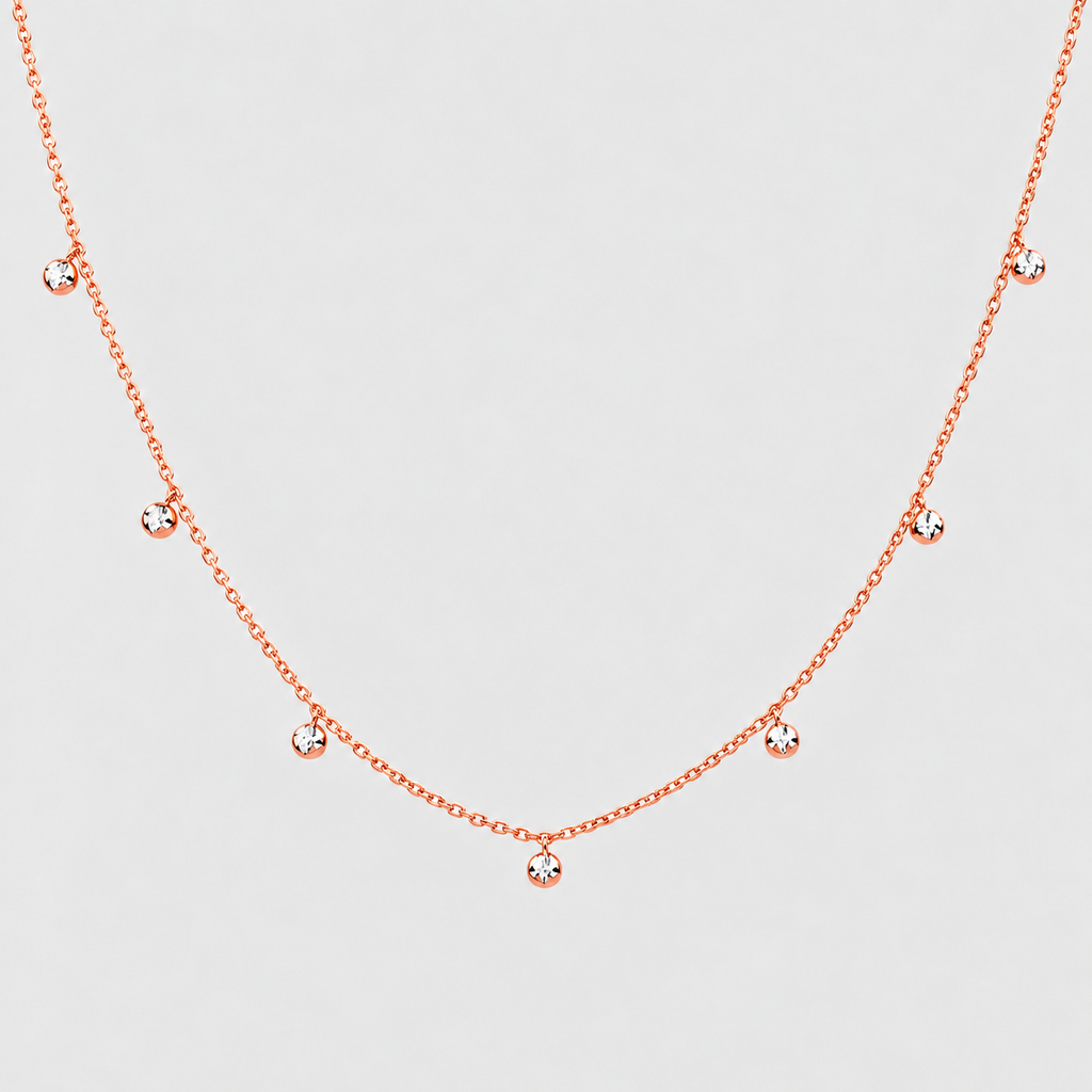 A delicate rose gold chain necklace featuring five small, clear round-cut gemstones spaced along the chain, displayed against a light gray background.