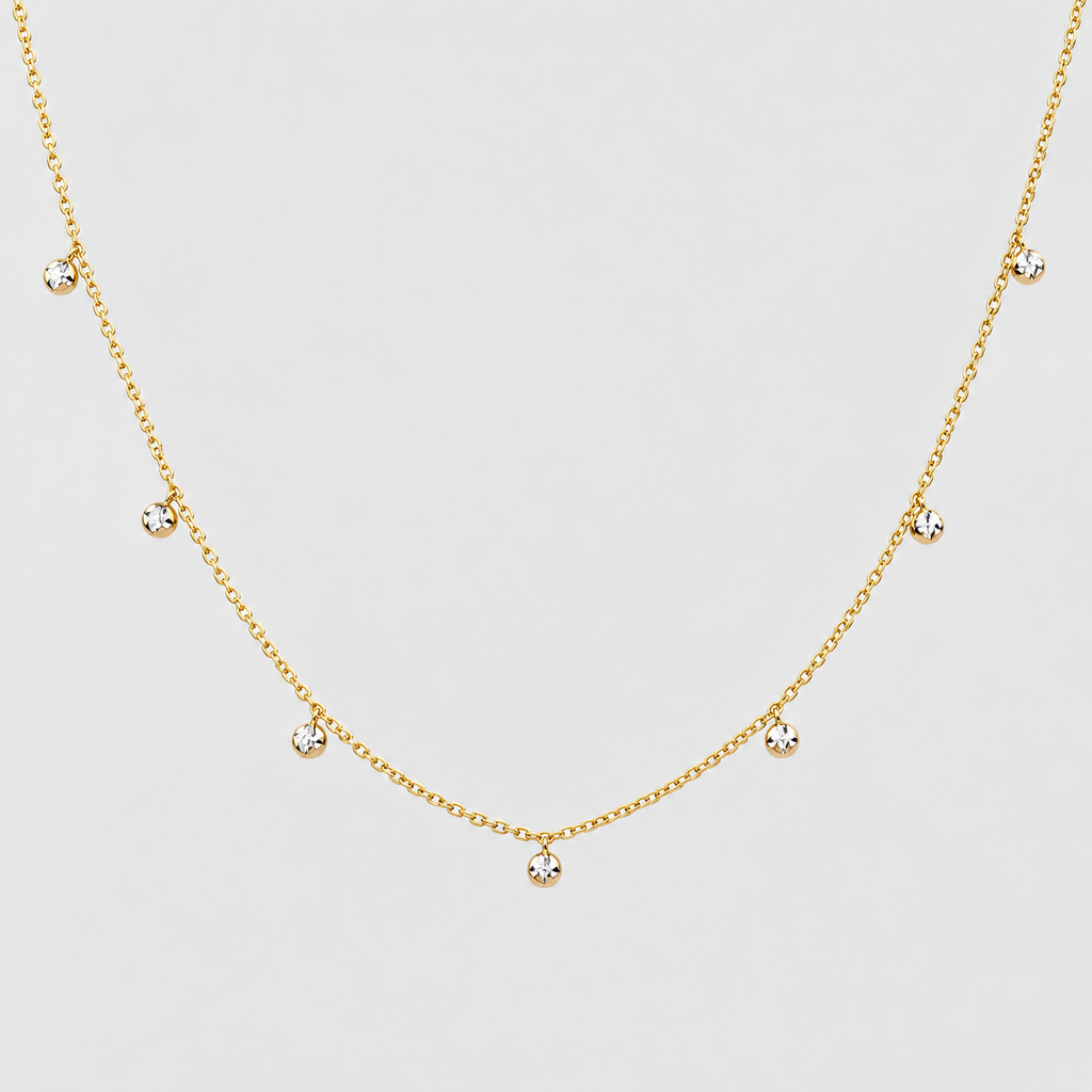 A delicate gold chain necklace featuring seven small, clear round-cut gemstones spaced evenly along the chain, displayed against a light gray background.
