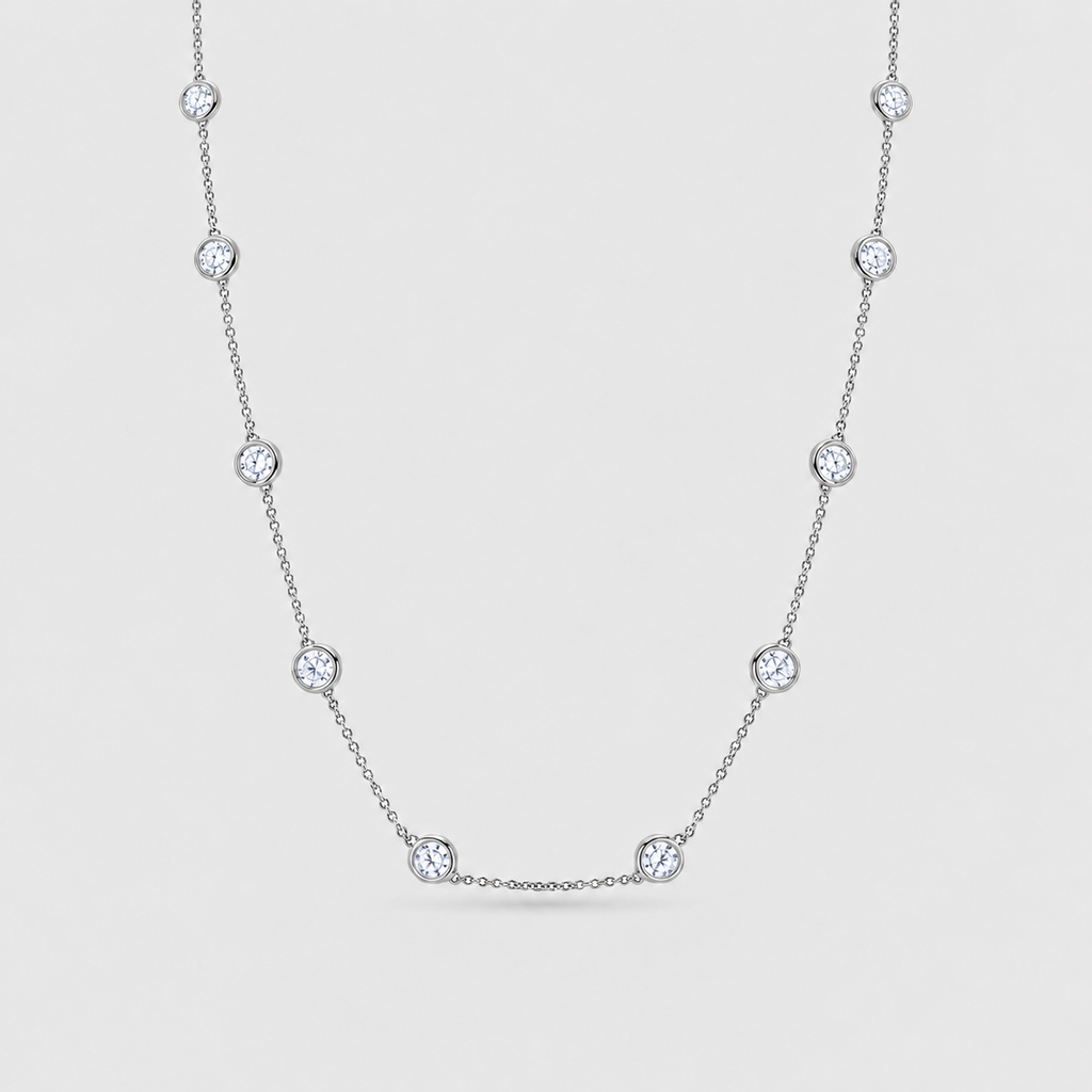 A delicate silver-toned chain necklace featuring seven evenly spaced round bezel-set clear gemstones, displayed against a light gray background.