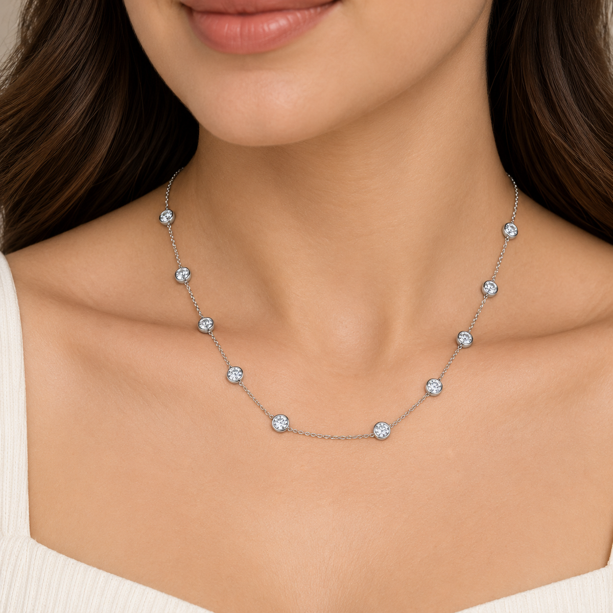 A close-up of a woman wearing a delicate silver chain necklace with multiple small, round, clear gemstone studs spaced evenly along the chain.