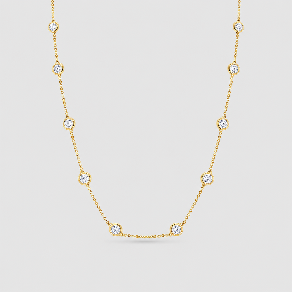 A delicate yellow gold chain necklace featuring nine small, bezel-set round clear gemstones spaced evenly along the chain, displayed against a light gray background.
