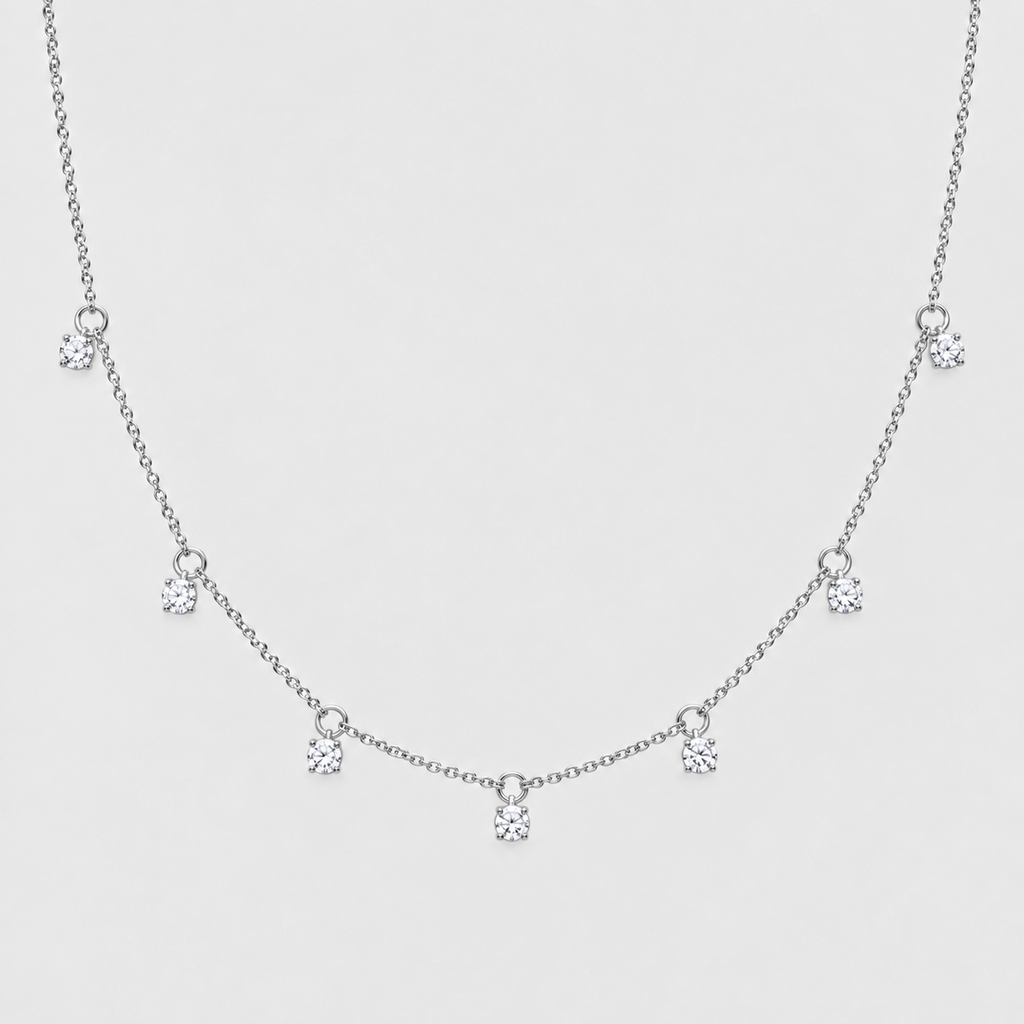 A delicate silver-toned chain necklace featuring five small, clear round-cut gemstones spaced along the chain, displayed against a solid light gray background.