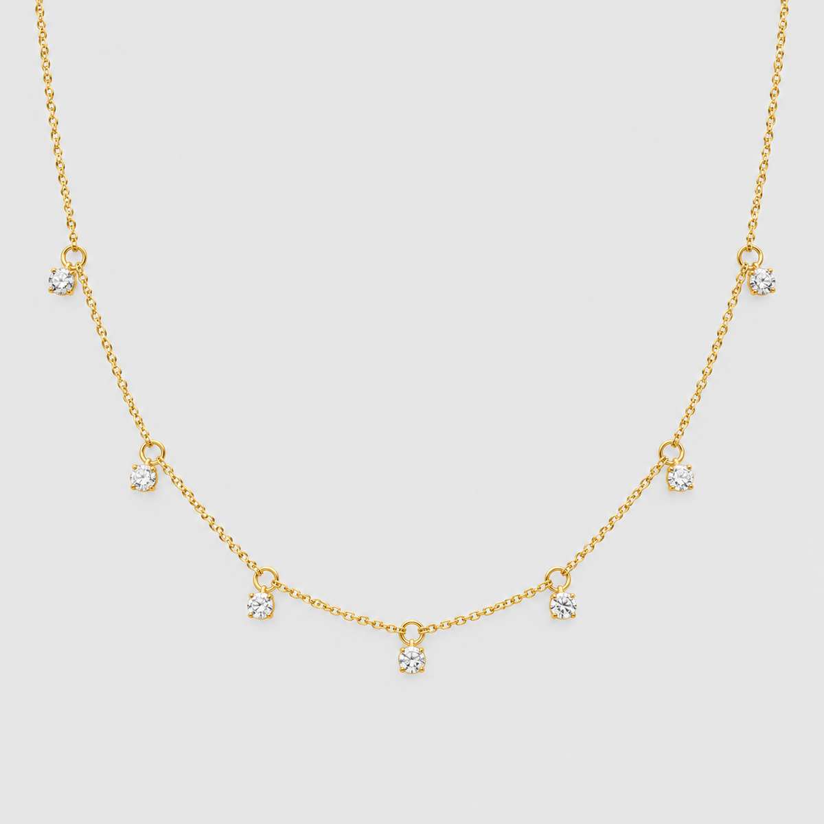 A delicate gold chain necklace featuring seven small, clear heart-shaped crystals spaced along the chain, displayed against a solid light gray background.
