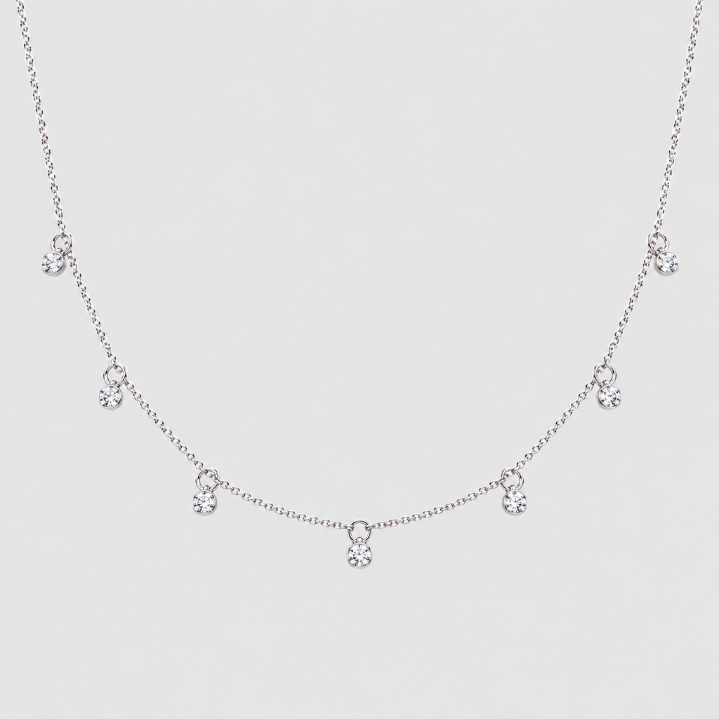 A delicate silver-tone chain necklace featuring five small clear crystal charms spaced along the front, displayed against a solid light gray background.