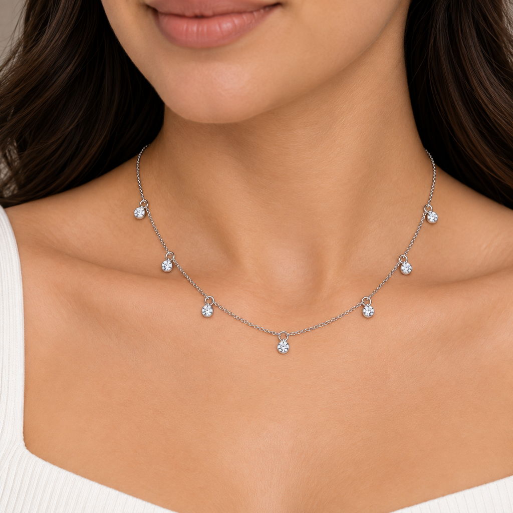 A close-up of a woman wearing a delicate silver-toned chain necklace with five small, clear gemstone flower charms spaced along the chain.