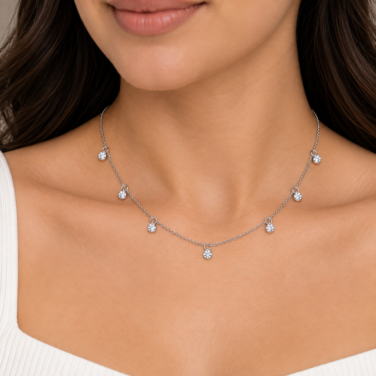 A close-up of a woman wearing a delicate silver-toned chain necklace with five small, clear gemstone flower charms spaced along the chain.