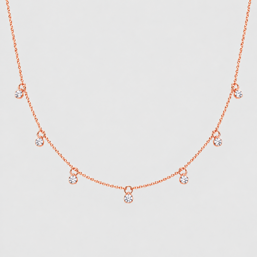A delicate rose gold necklace featuring a fine chain with small, spaced-out teardrop-shaped crystal charms, displayed against a light gray background.