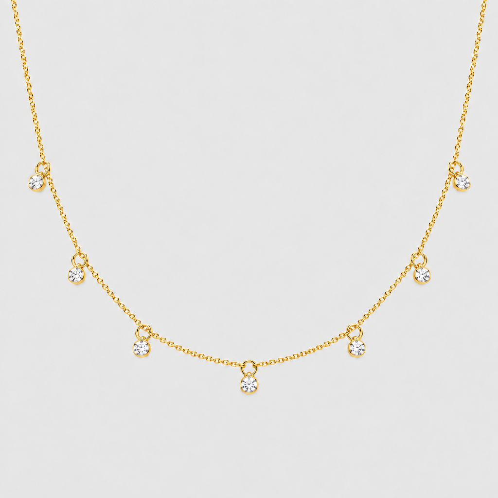 A delicate gold chain necklace featuring five small, clear round-cut gemstones spaced along the chain, displayed against a light gray background.