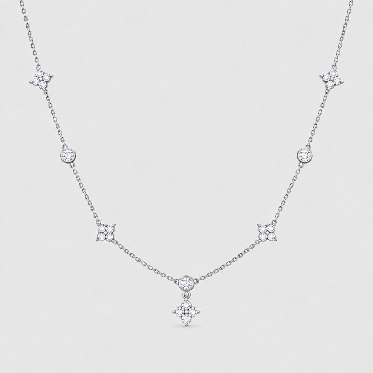 A delicate silver-toned necklace featuring a central diamond-shaped pendant and five matching starburst motifs spaced along the chain, displayed on a light gray background.